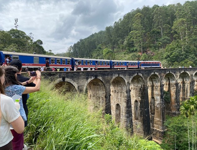 Der Zug fährt über die historische Eisenbahnbrücke bei Ella. Viele Touristen schauen dem Spektakel zu.